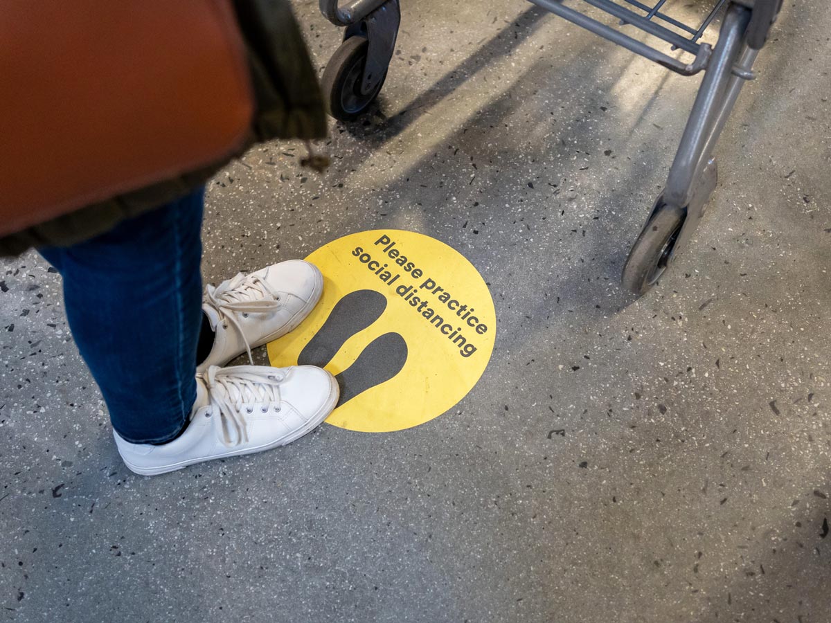 A woman stands on a floor decal that reads "please practice social distancing"