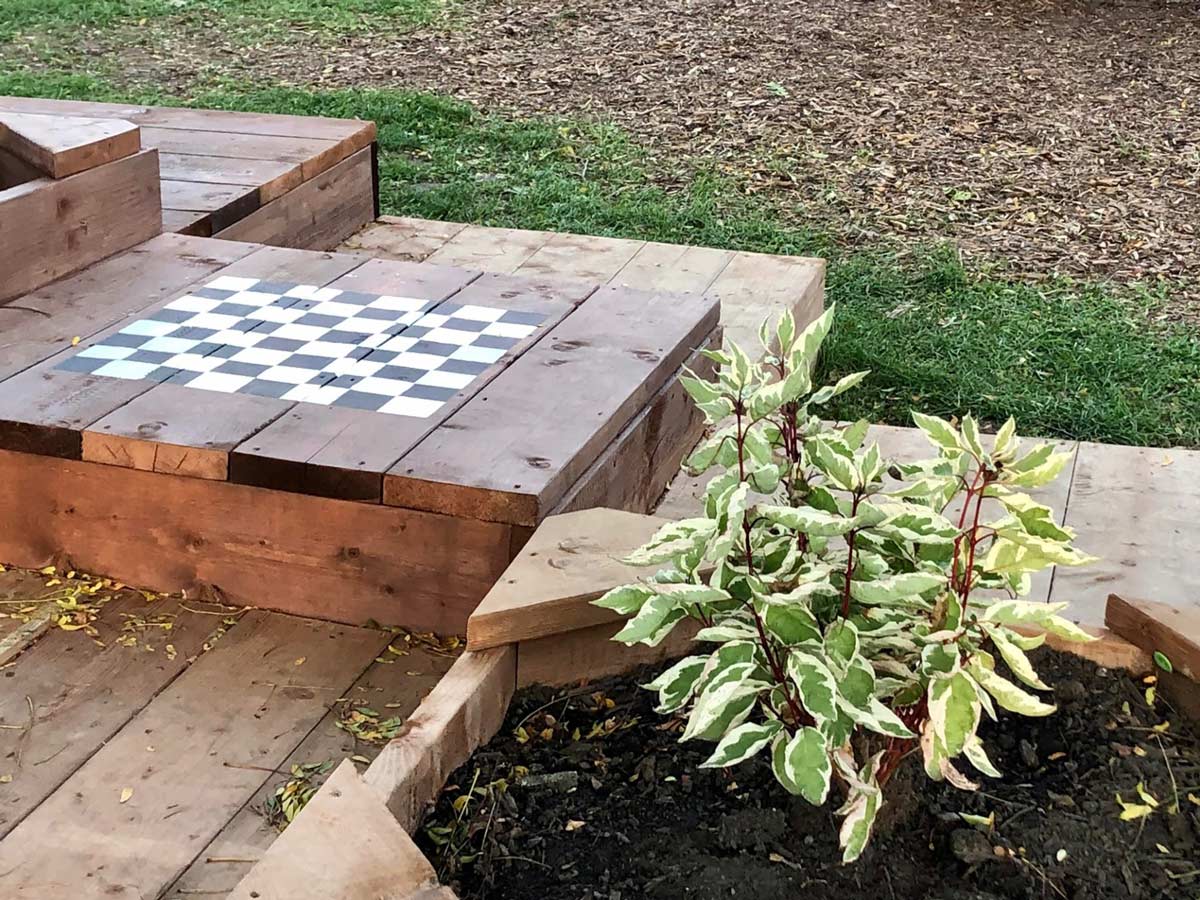 A wooden chessboard, seating area and plant as part of a new playground design.