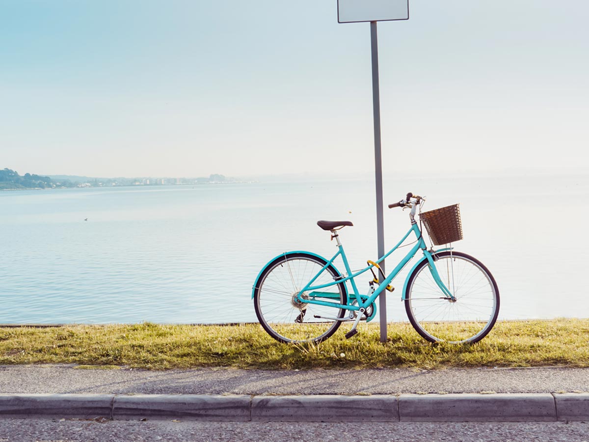 A blue bicycle propped up on a sign in front of a body of water. 