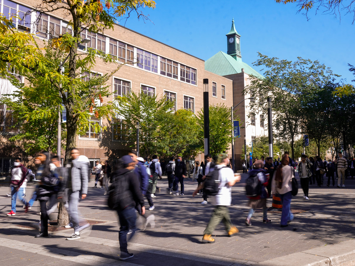 Crowds of people walk along a tree-lined Gould Street on the TMU campus on a sunny day. In the background are the library and Kerr Hall buildings. 