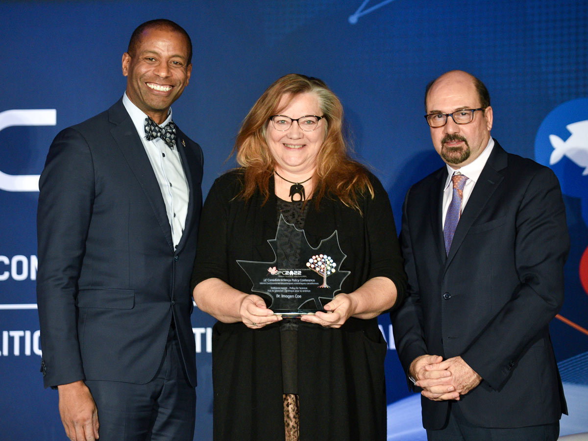 Professor Imogen Coe (centre) holds a glass maple leaf shaped award at the CSPC annual conference award ceremony. She is pictured with MP Greg Fergus (left) and CSPC CEO and President Mehrdad Hariri (right).