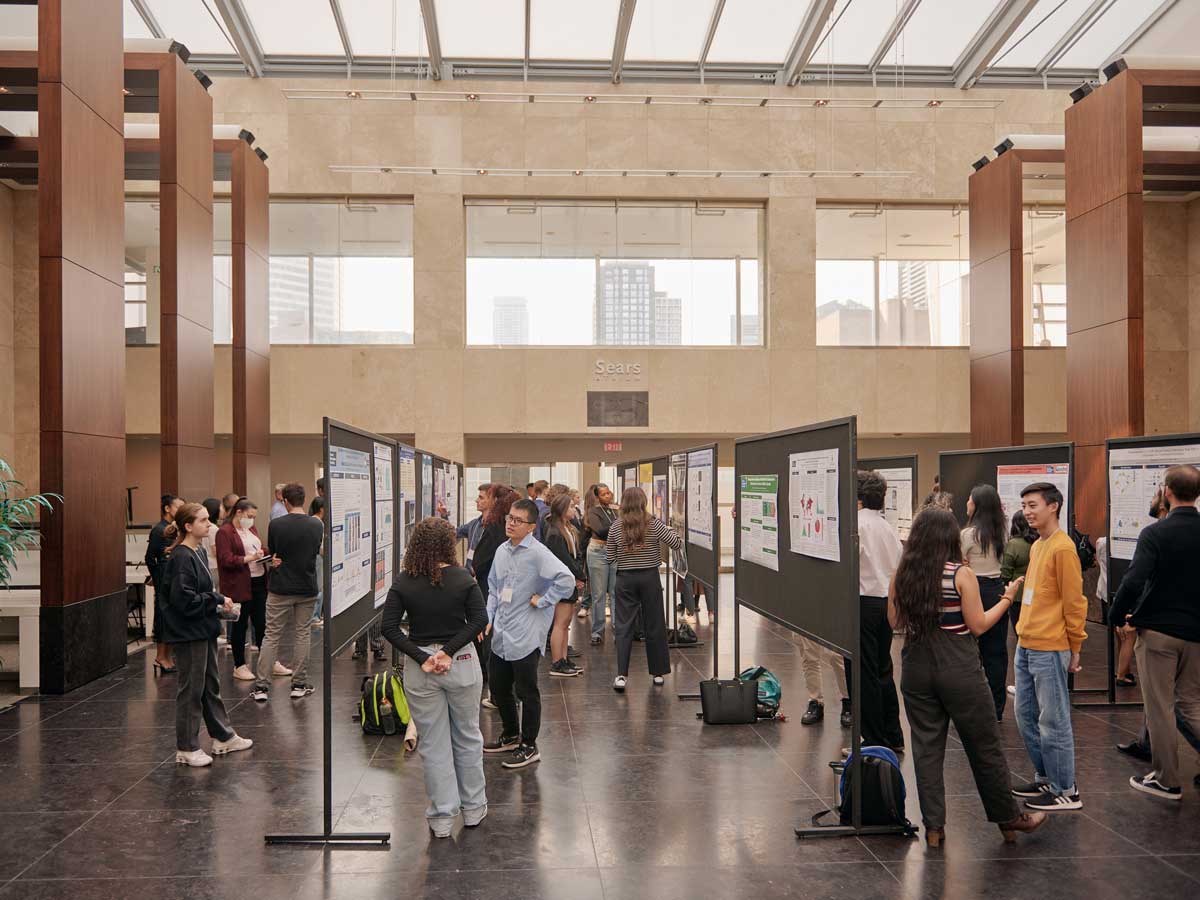 Students and showcase attendees circulate a large room examining the dozens of research posters. 