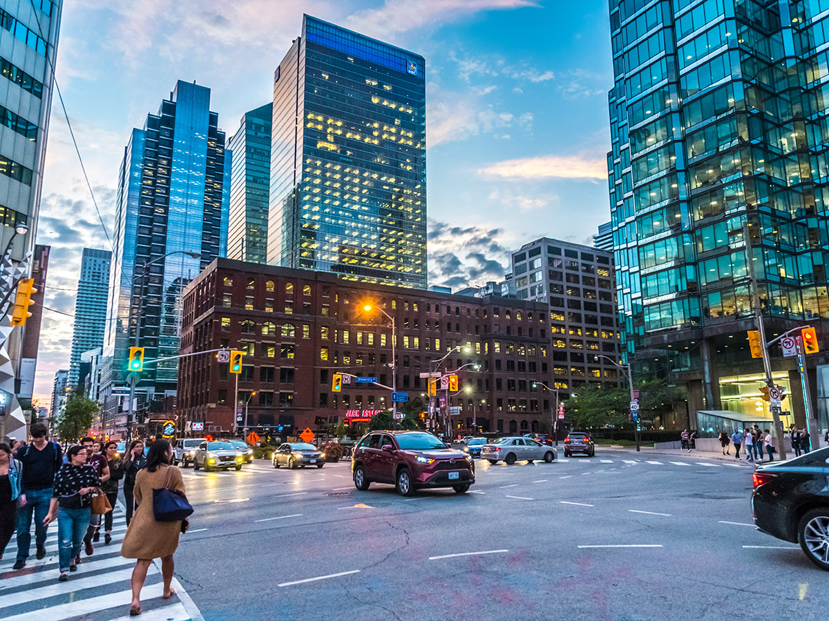 A busy downtown Toronto intersection with pedestrians crossing the street, cars turning and city buildings in the background