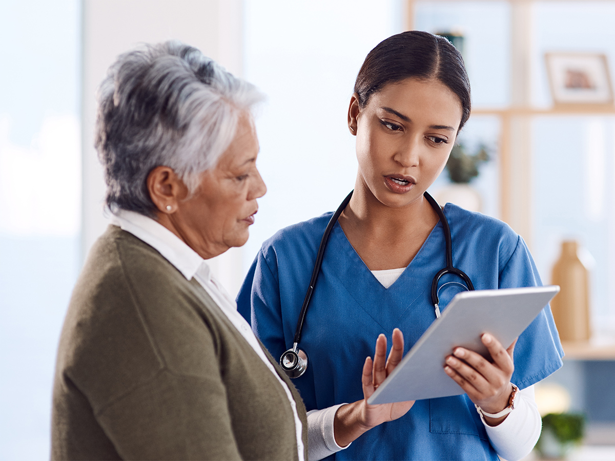 A female doctor wearing blue scrubs speaks with a female patient