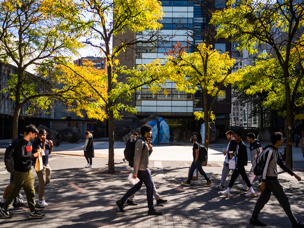Students walk outside on the TMU campus during the daytime with yellow leaves on surrounding trees.