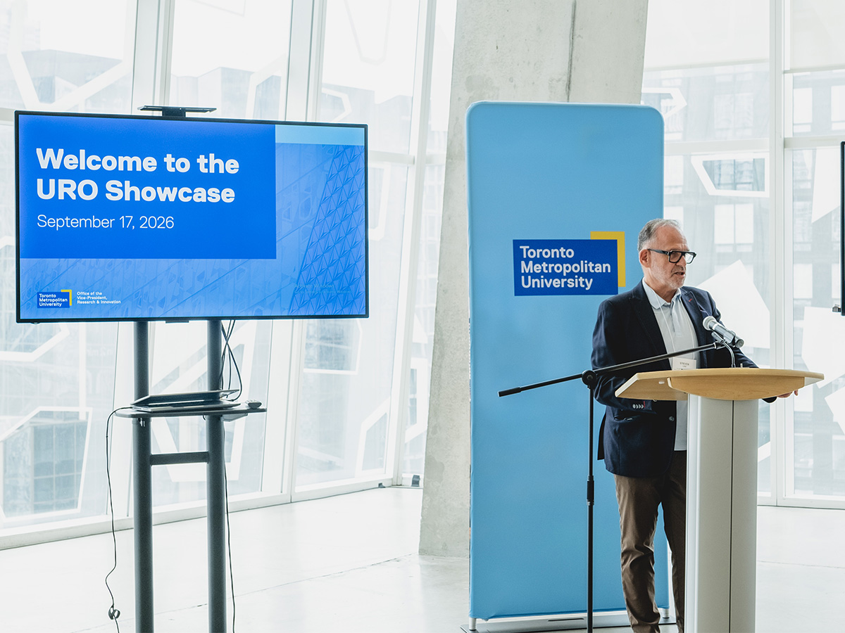 Steven N. Liss stands at a podium speaking into a microphone in front of a wall of windows and a Welcome to the URO Showcase sign