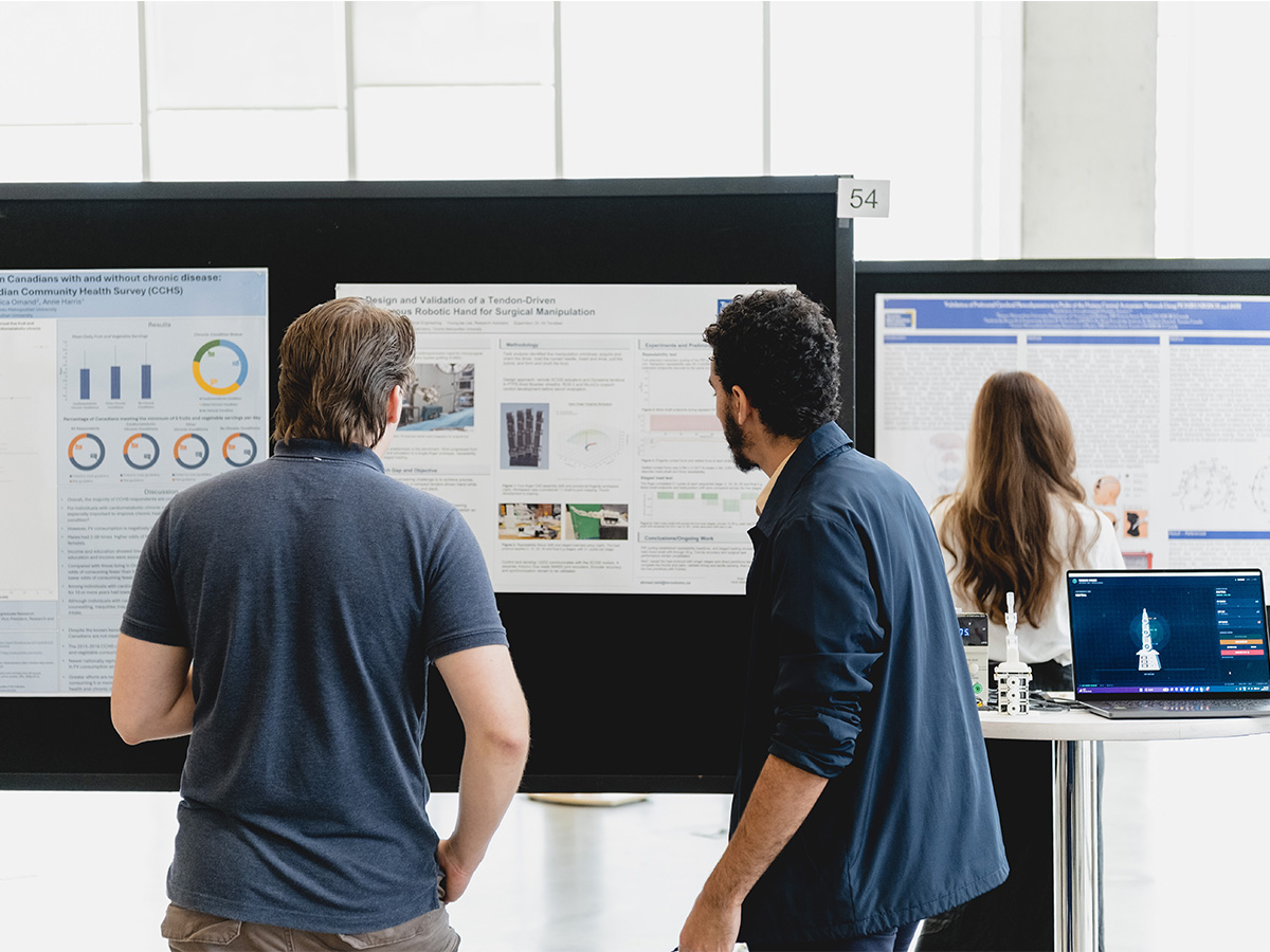 Two students stand with their backs to the camera looking at a research poster