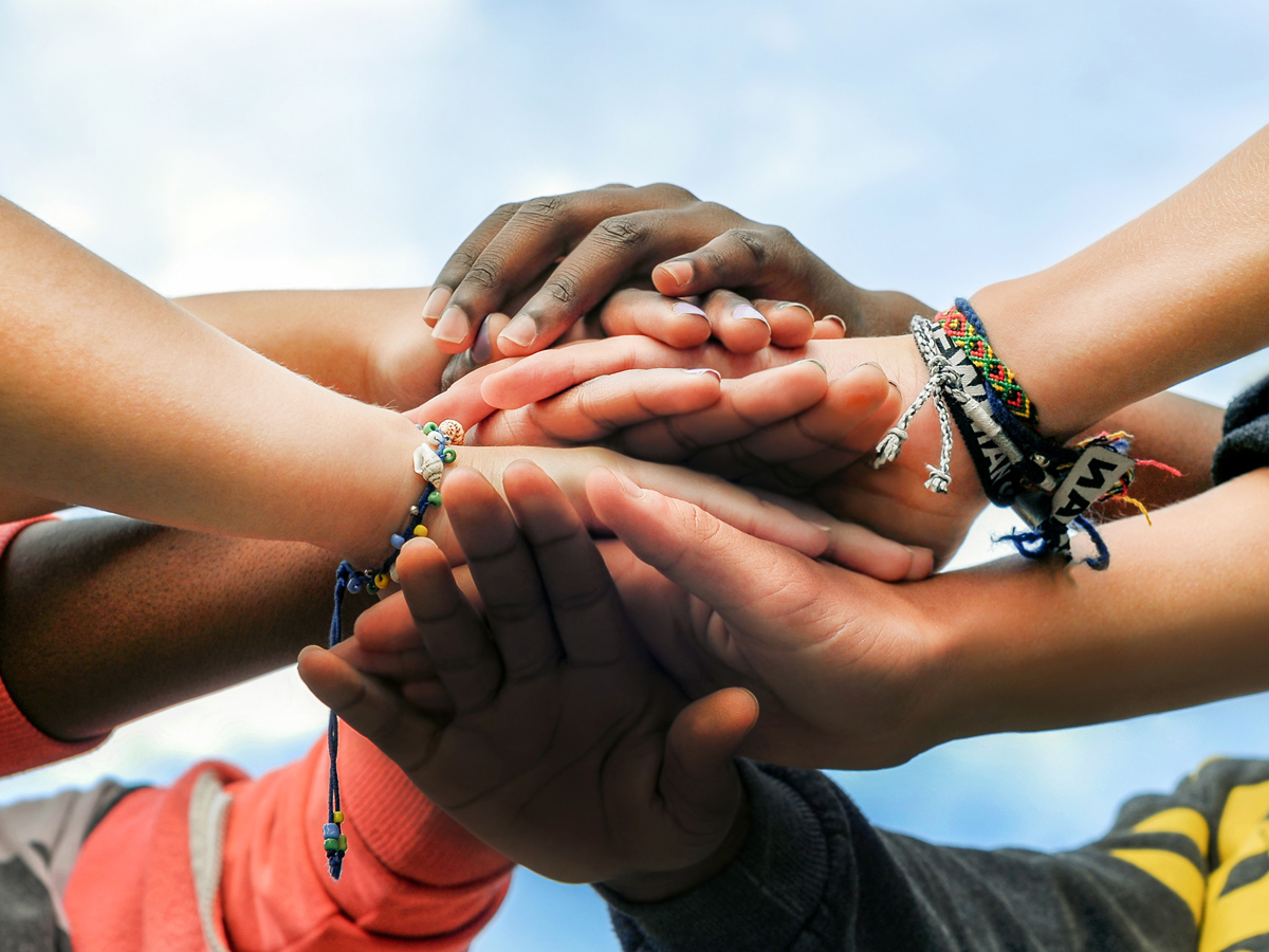 A close up shot of the clasped hands of a multicultural group of youth
