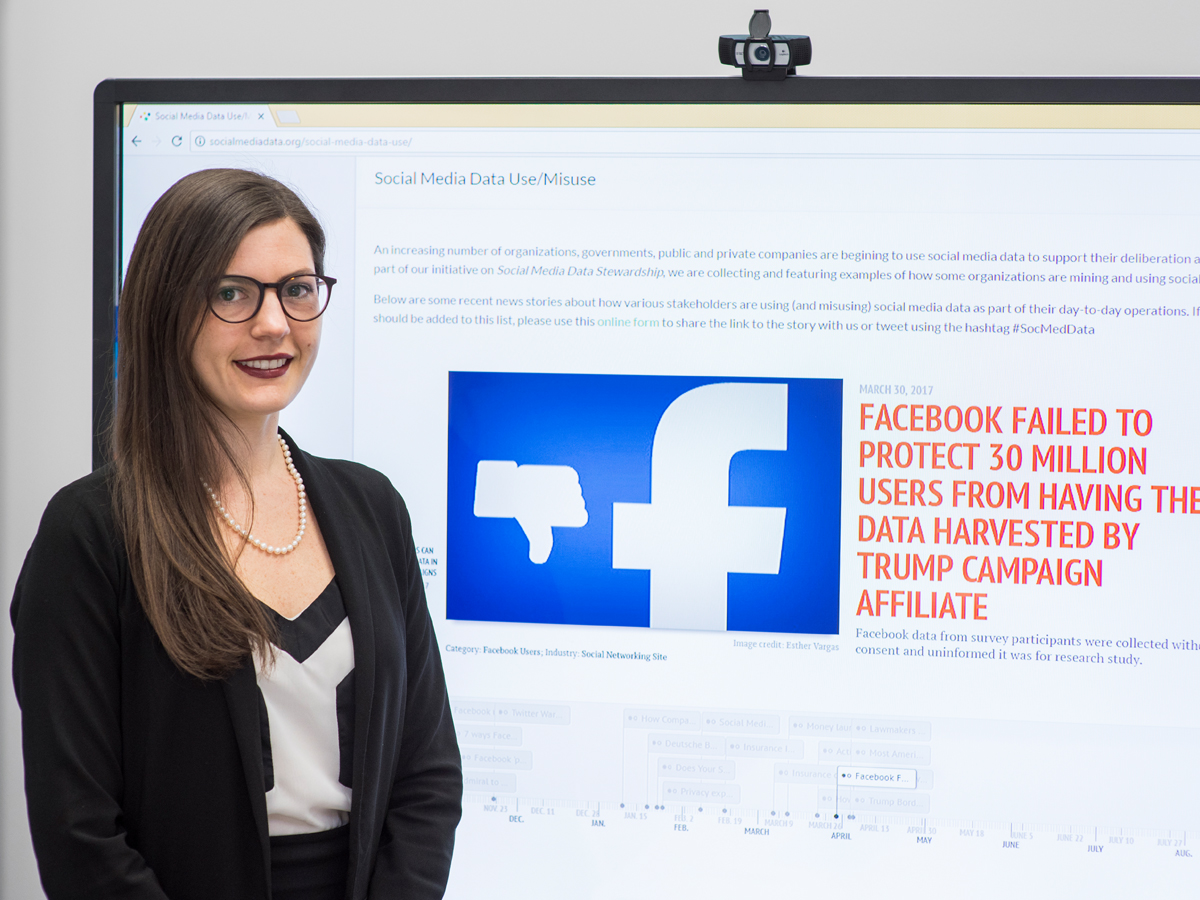 Postdoctoral fellow Jenna Jacobson stands in front of a projector screen that reads "Facebook failed to protect 30 million users from having their data harvested by Trump campaign affiliate"