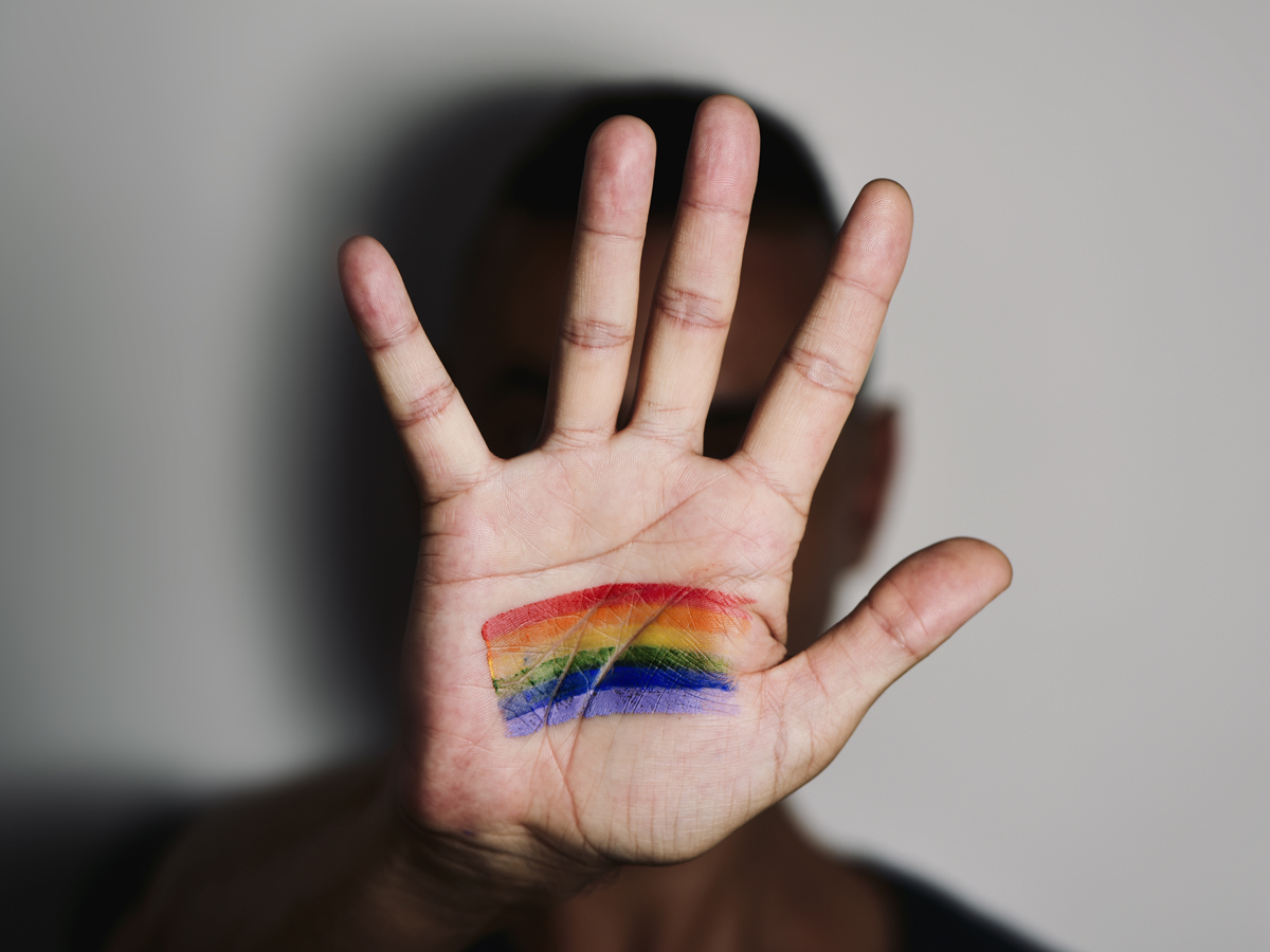 An unidentified person holds up a hand with a rainbow painted on their palm
