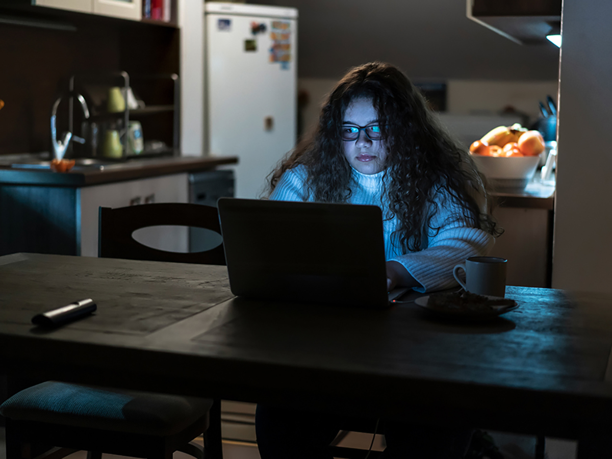 A university-aged woman works on her laptop at a kitchen table