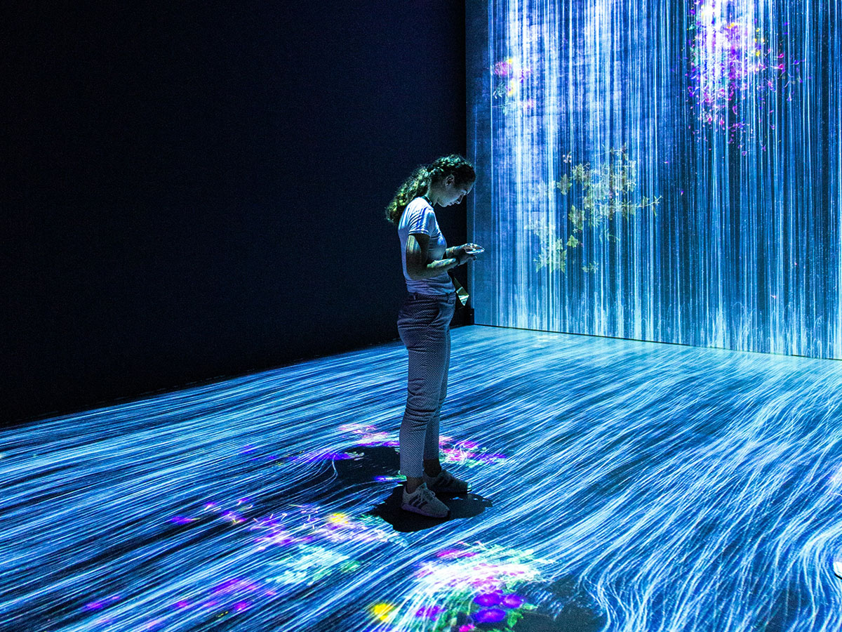 A woman stares at her smart phone in a room filled with projections of light