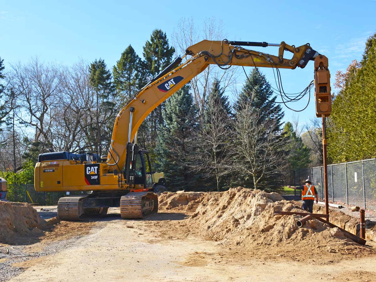 A construction site where heavy equipment is being used to drive metal poles into the ground.