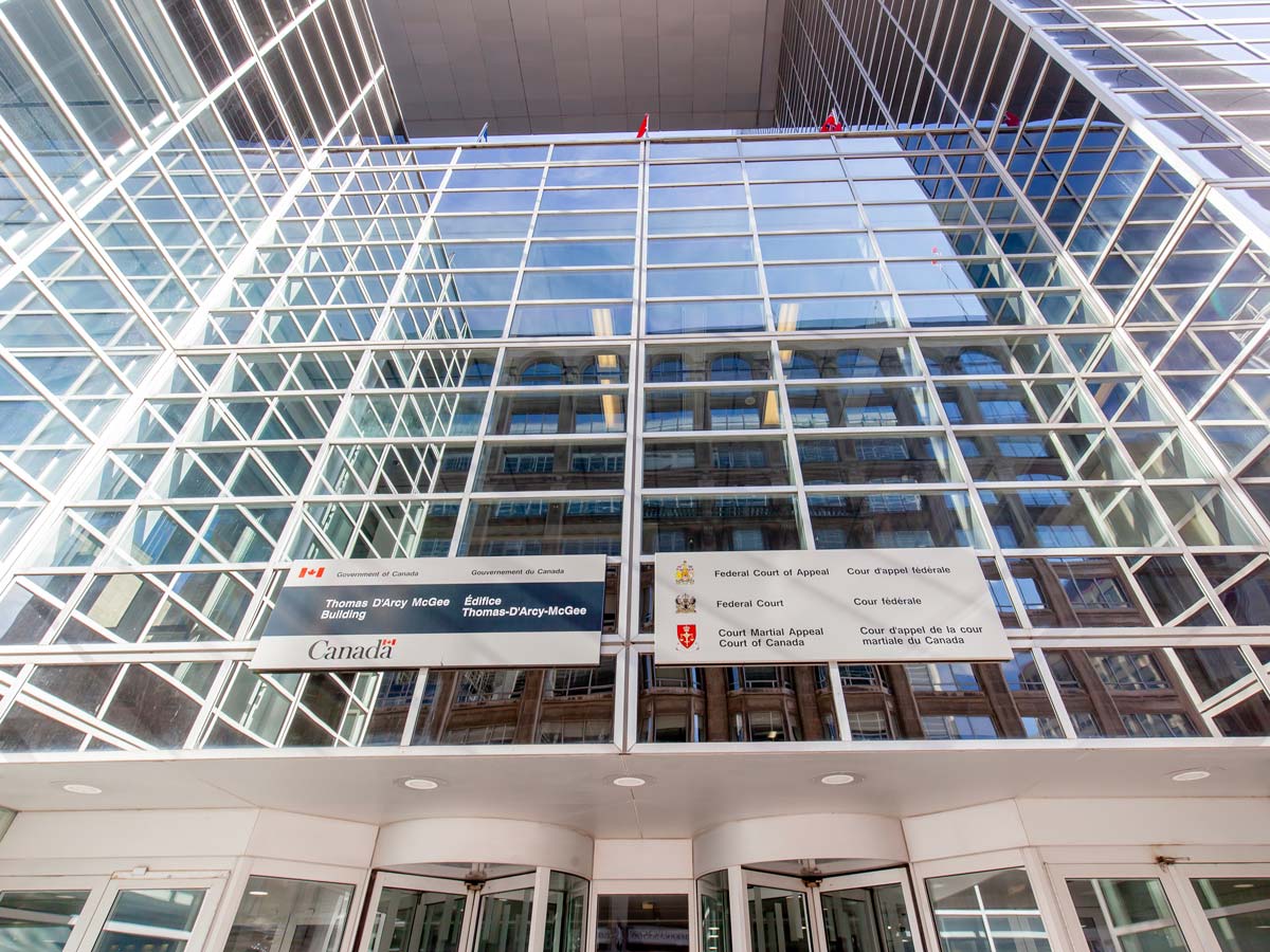 The front of the Thomas D'Arcy McGee Building, which is mostly glass, with flags and government signage above the entrance.