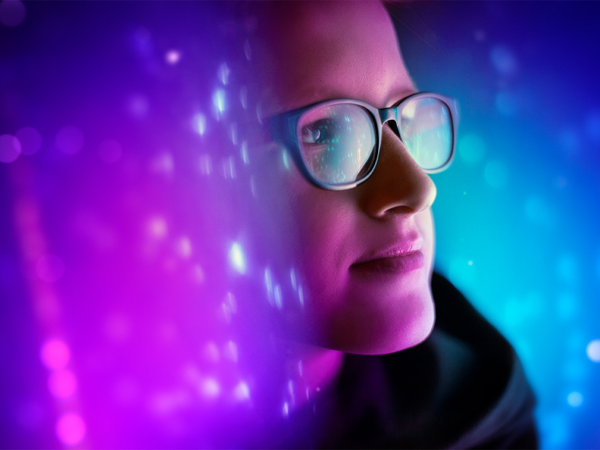 A profile of a person’s face wearing glasses surrounded by blue and pink light with white dots.