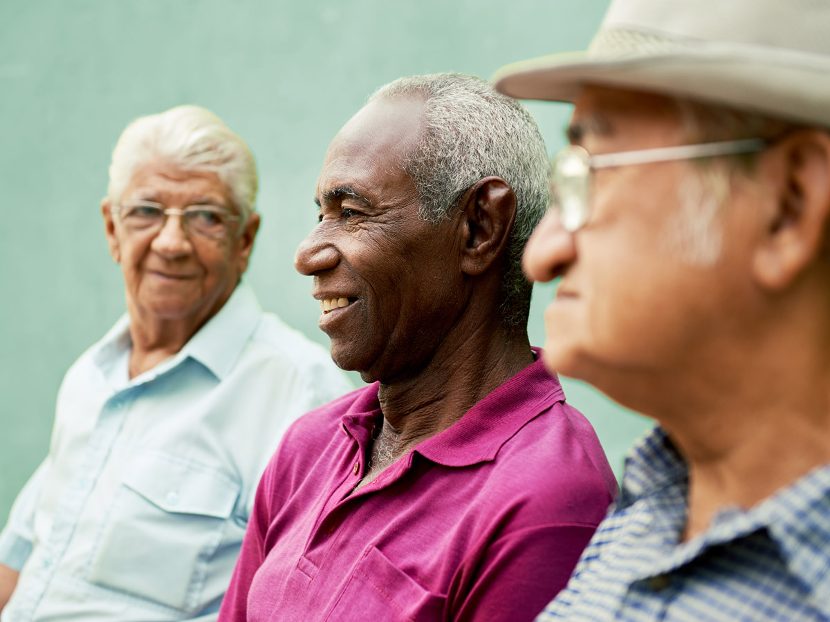 Three male, older racialized adults interact against a green background