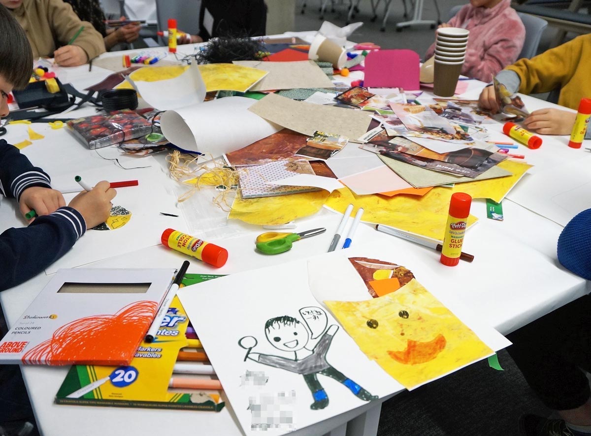 Children seated around a table, drawing pictures of themselves and creating collages representing the contents of their lunch bags