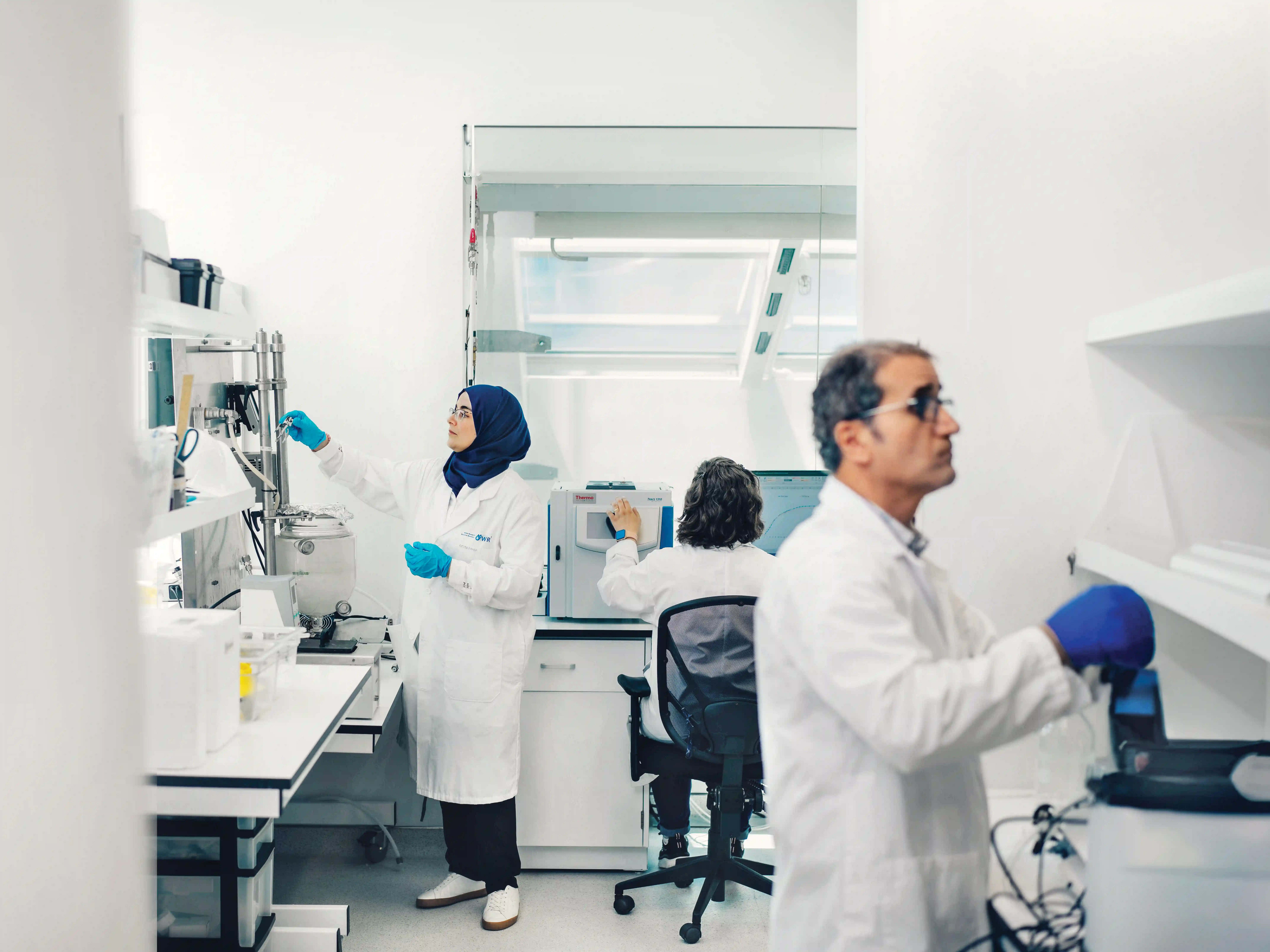 Three scientists wearing white coats work in a lab