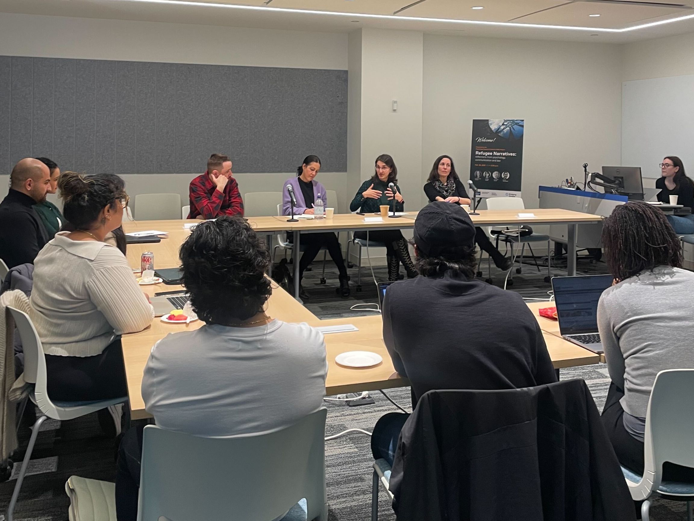 Mutiple people, including professors and students, sitting in a meeting room while engaging in a group discussion.