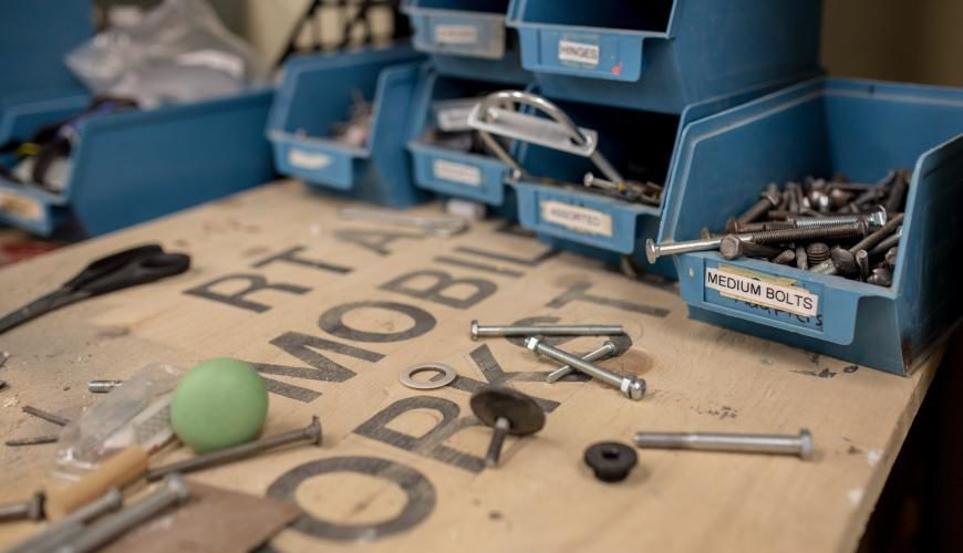 Pictured is a table in the workshop with bolts and other supplies scattered and in containers 