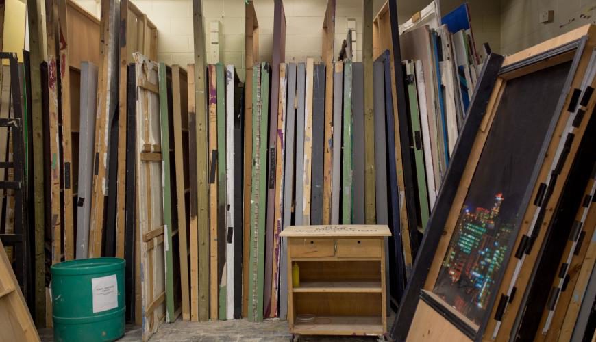 Pictured are backdrops for various production sets standing upright in the prop room