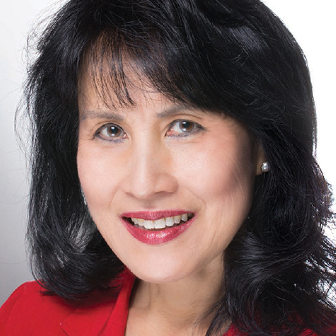 Close-up headshot of Jennifer Lynn smiling. She has long dark hair and is wearing a red blazer.