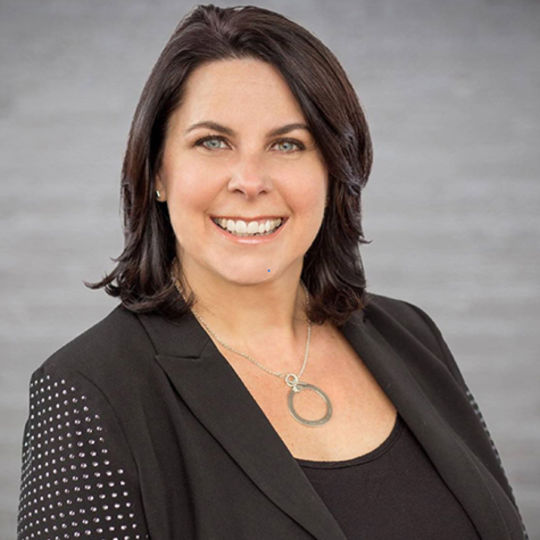 A close-up headshot of Michelle Melanson, smiling, with dark brown hair, wearing a black jacket over a dark top.