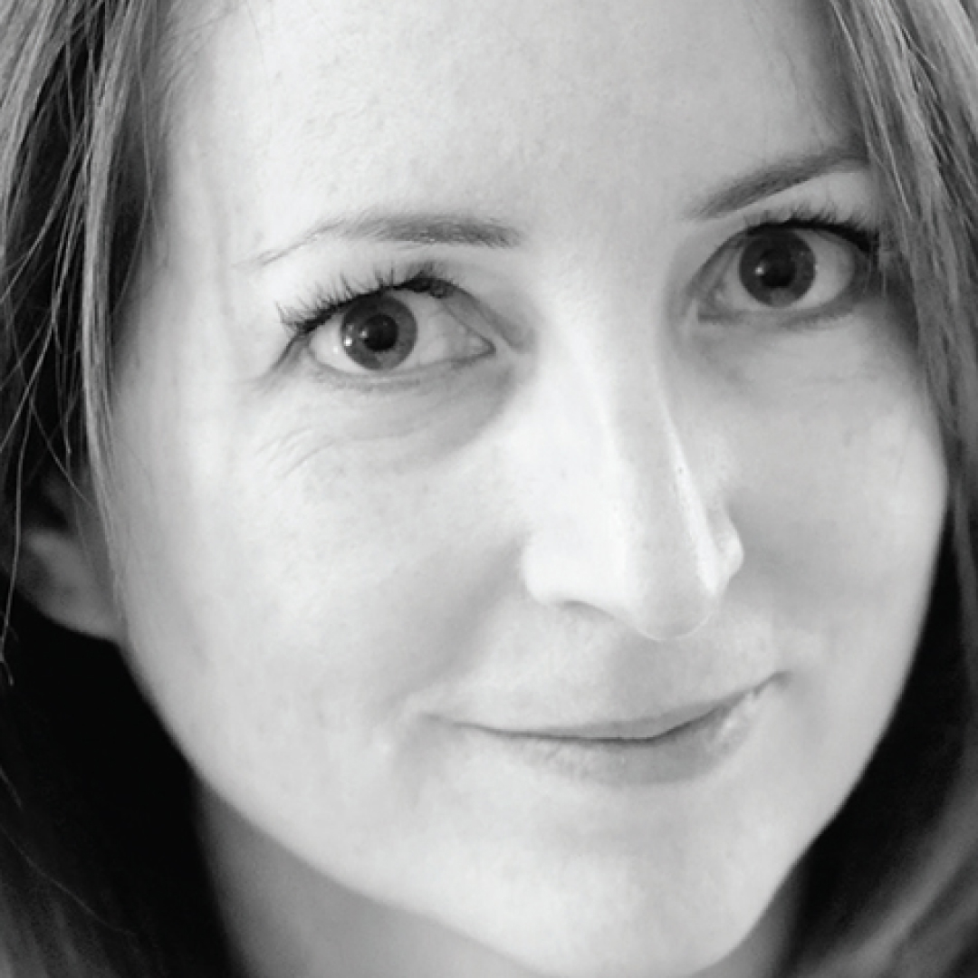 A black-and-white close-up headshot of Tracey Forbes. She has light straight hair and is smiling softly with a calm expression.