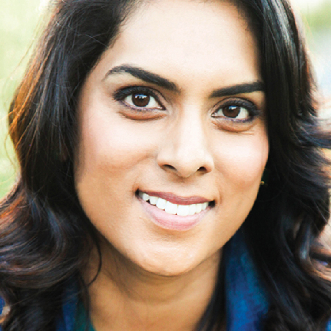 A close-up headshot of Vera Santamaria. She has medium-length dark brown hair styled in loose waves and dark eyes. She is smiling and wearing a dark blue top.