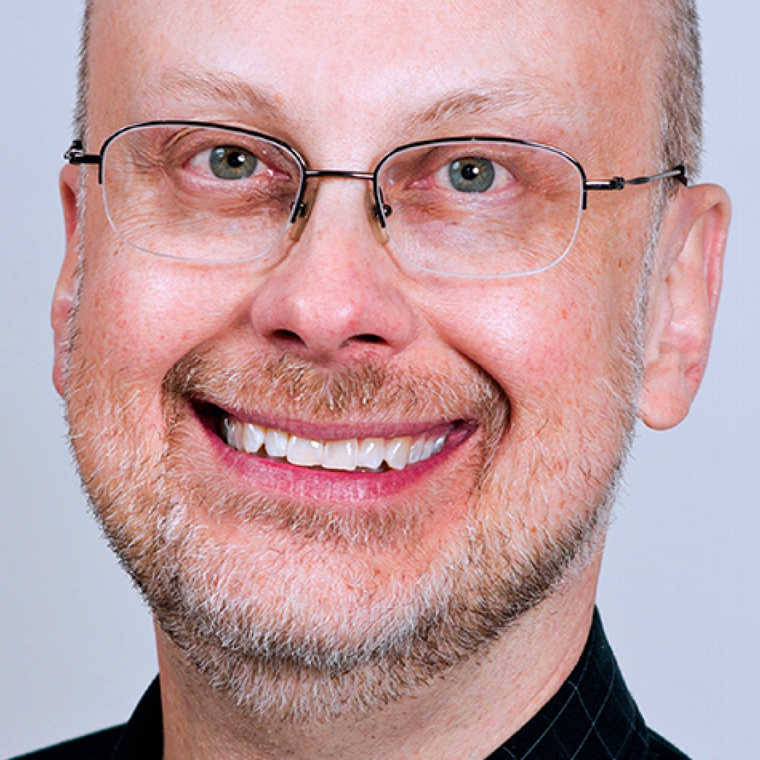 A close-up headshot of Robert J. Sawyer. He has a light beard and mustache, wears thin glasses, and is smiling warmly at the camera.