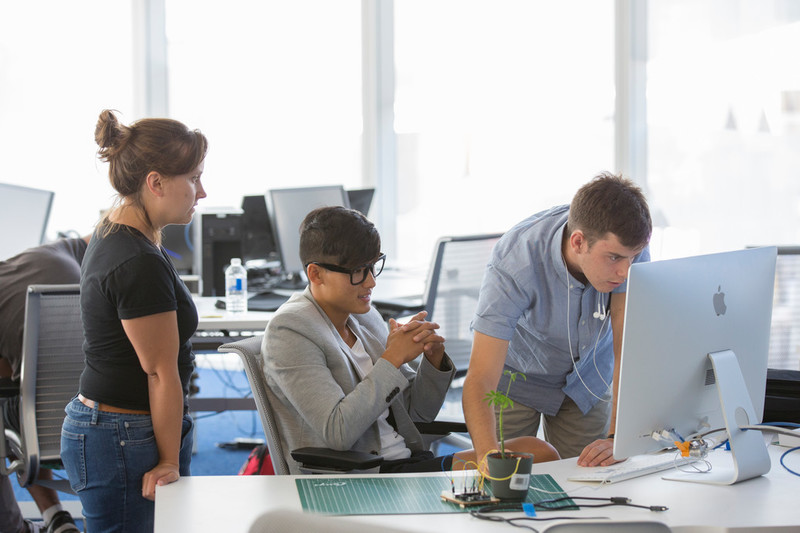 Pictured are 3 students/staff members working on a computer to fix the code for an electronics project
