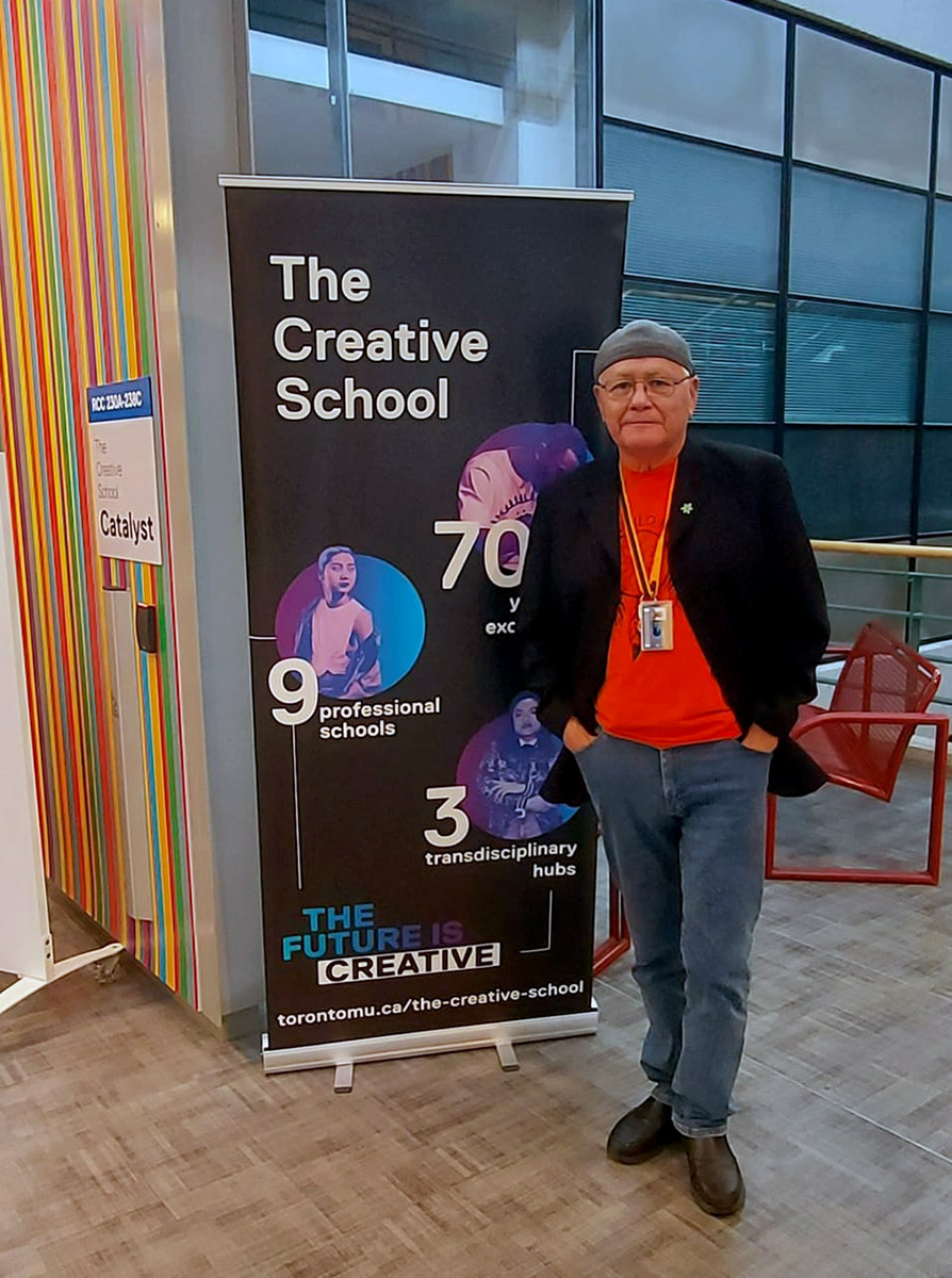 Dr. Michael Doxtater, Director Saagajiwe poses in an orange shirt in front of a  Creative School sign