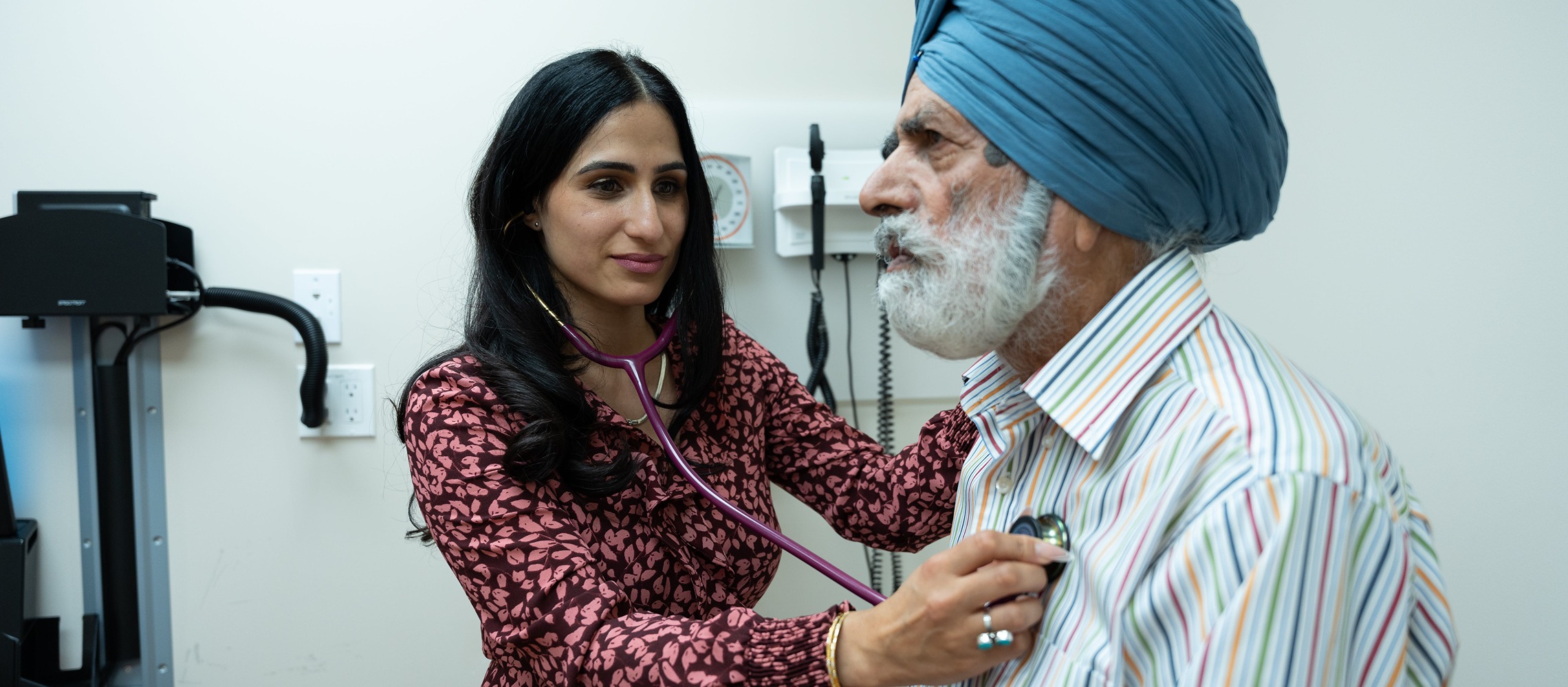 A female doctor listens to the heart of an elderly male Sikh patient