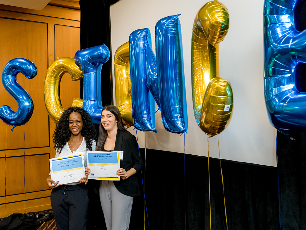 Two smiling students holding award certificates in front of balloons that spell out Science