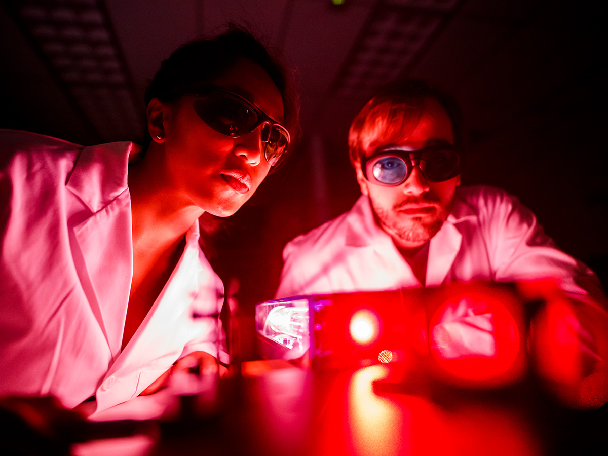 Medical physics students in red-lit lab working with lasers