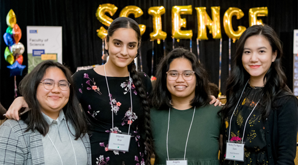 Four students smiling with science balloons in the background