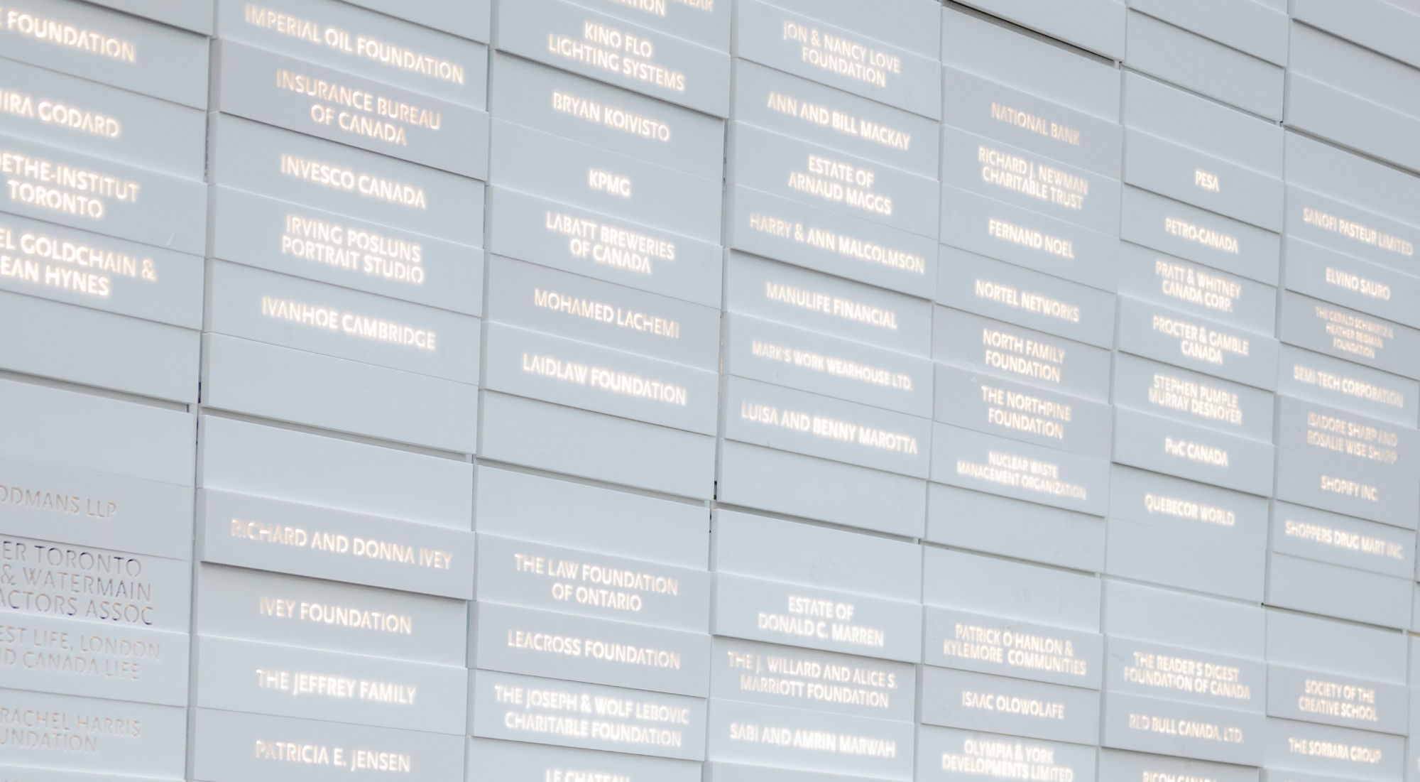 Wall of donor plaques listing individual, corporate, and foundation names on grey tiles