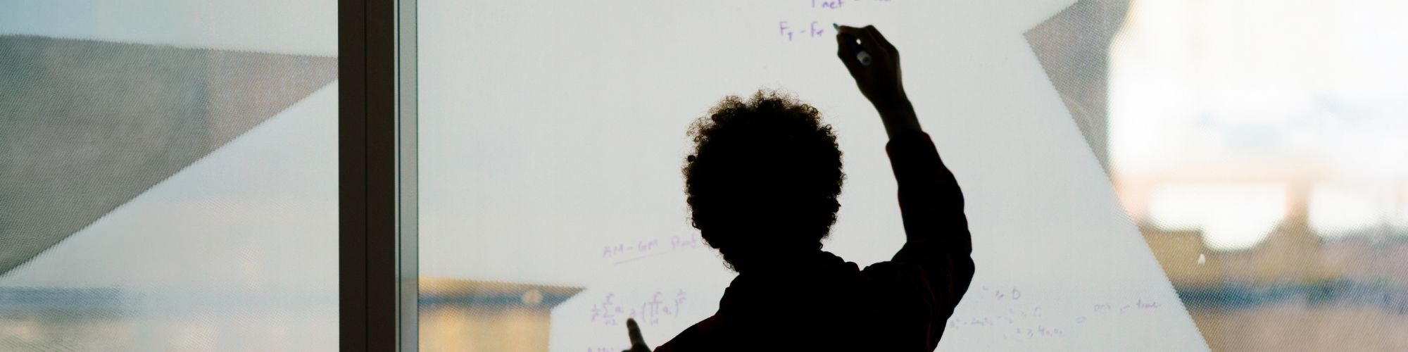 Silhouette of student writing math equations on a glass