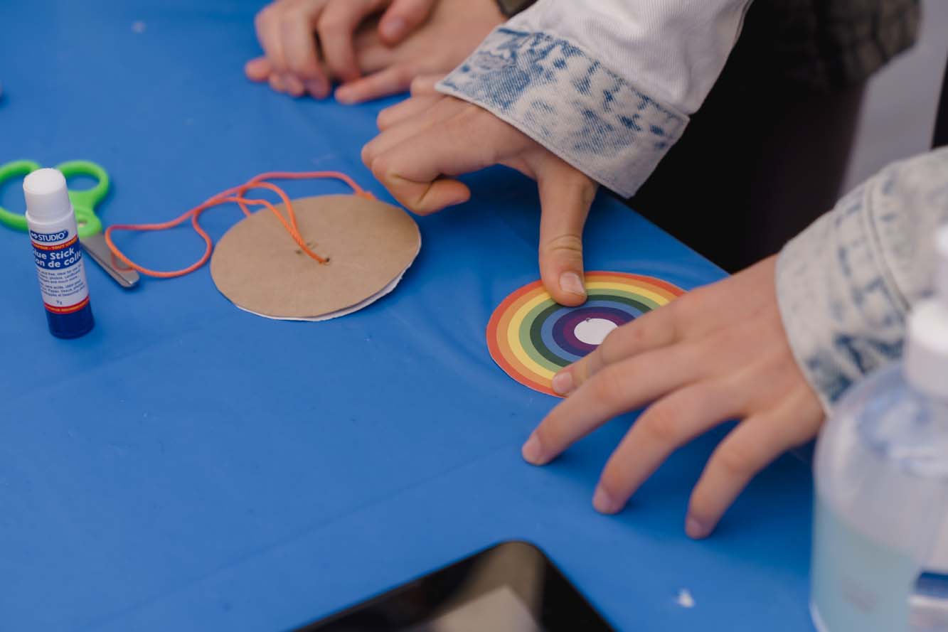 A child puts a rainbow-coloured paper circle on the table.