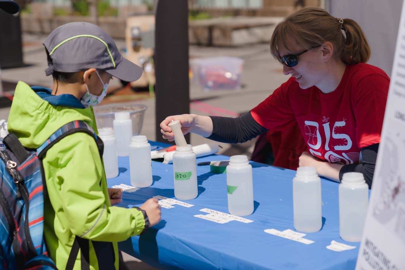 A volunteer puts a plastic tube into a water sample in a bottle labelled 620 as a child watches.