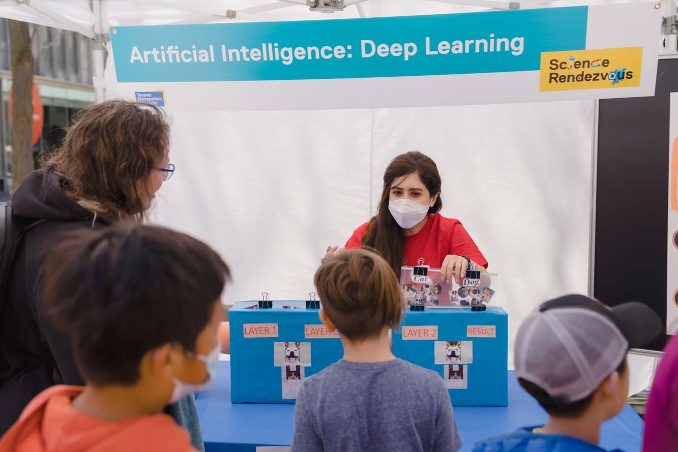 A volunteer holding a plastic folder with photos of cats and dogs from a blue box at the Artificial Intelligence: Deep Learning booth.