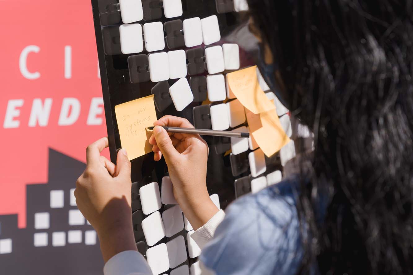 A participant writing on an orange Post-it note on a board.