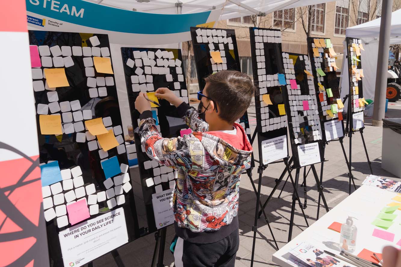 A child putting up a Post-it note on a board at the STEAM booth.