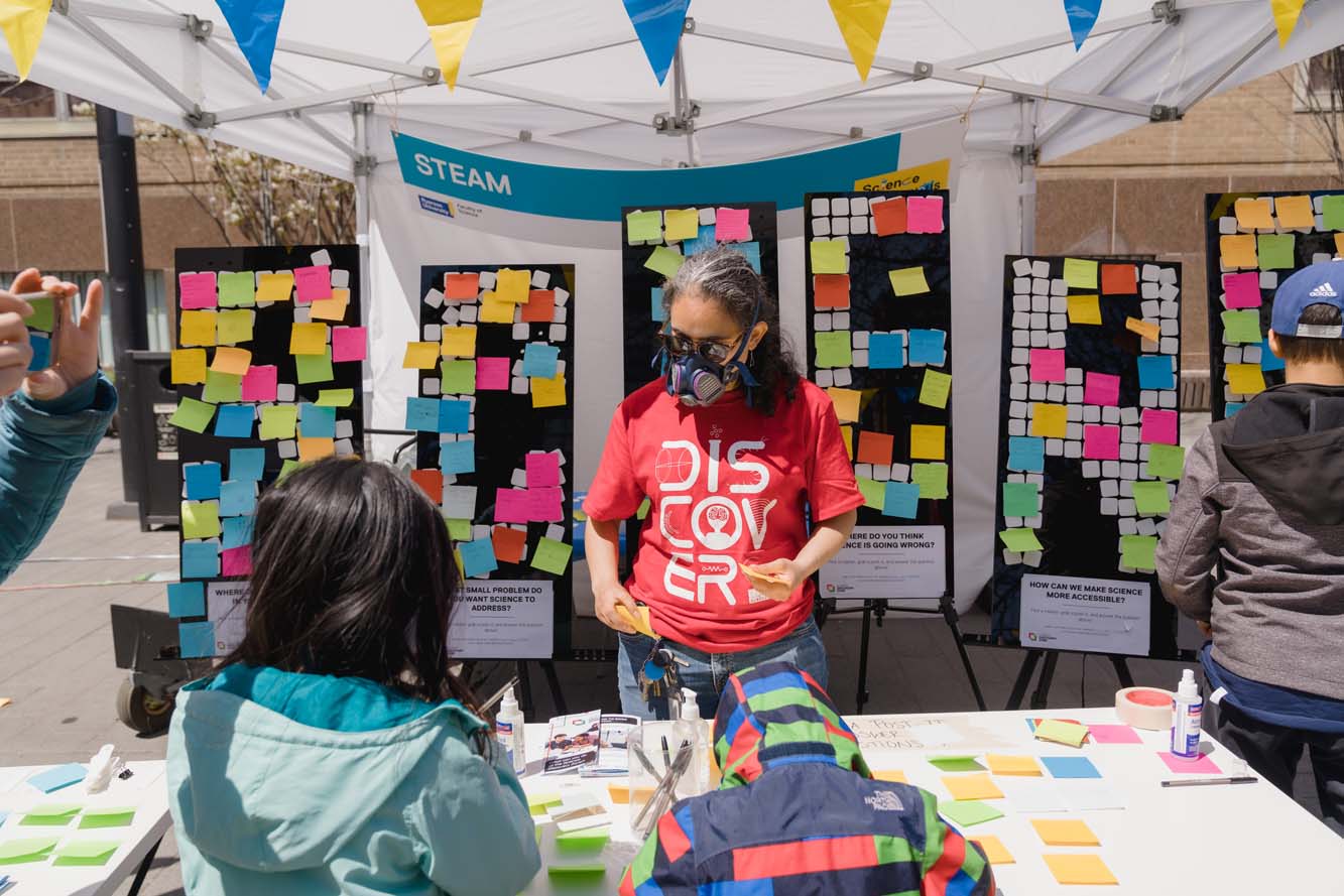 A volunteer holding Post-it notes while two children are at the STEAM booth