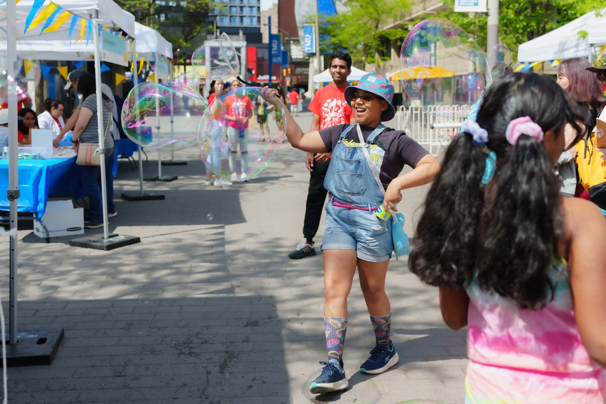 A kid smiling while making multiple giant bubbles on the street.