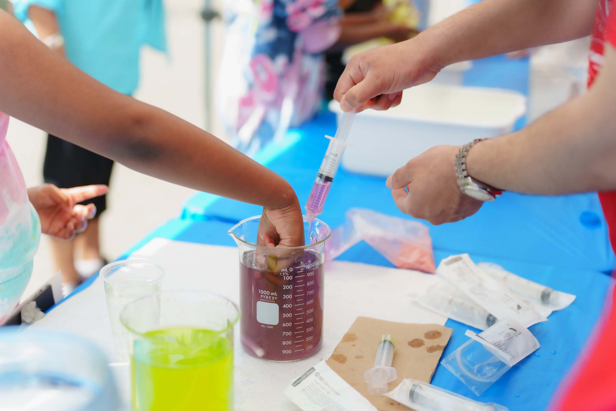 A child puting his or her hand in a beaker filled with purple liquid at the Food Science booth after a volunteer extracted the liquid from the beaker. 