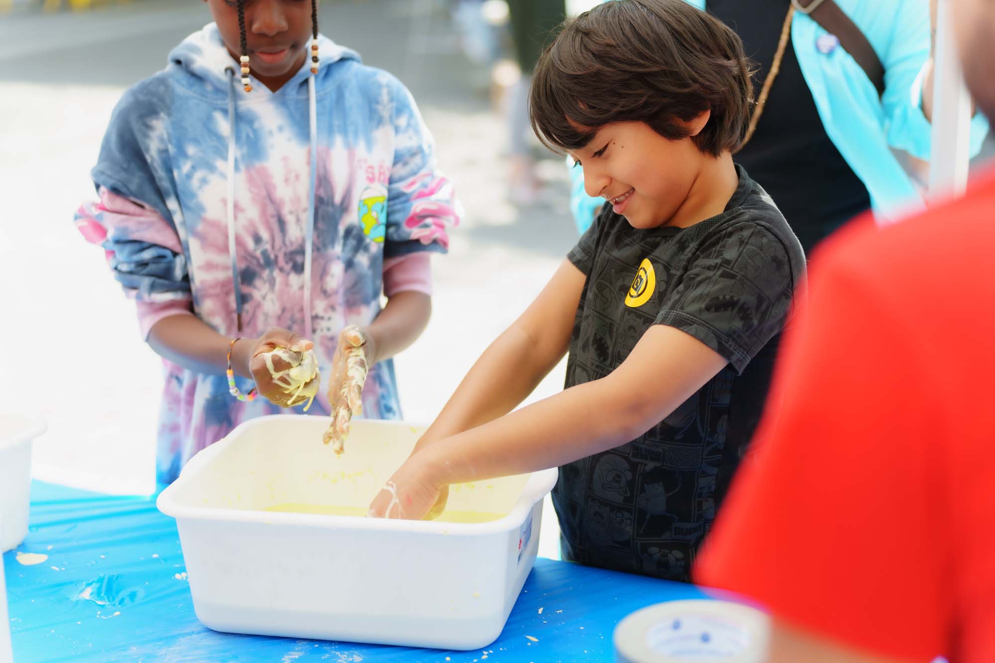 Two children playing with the yellow slime in a white container.