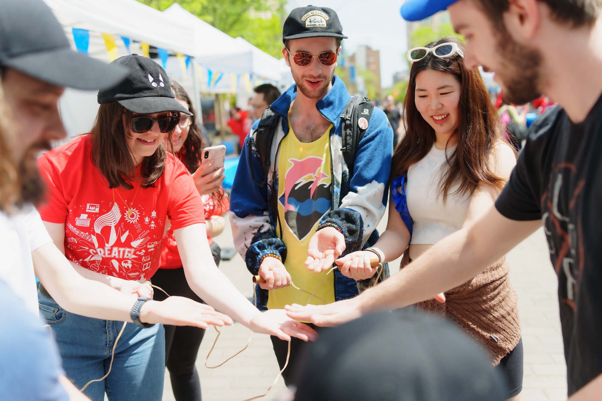 Volunteers engaging with participants in an activity called "Human Piano" where they each hold onto a metal device with one hand. As they tap on the other's empty hands, they complete a circuit and create sound.