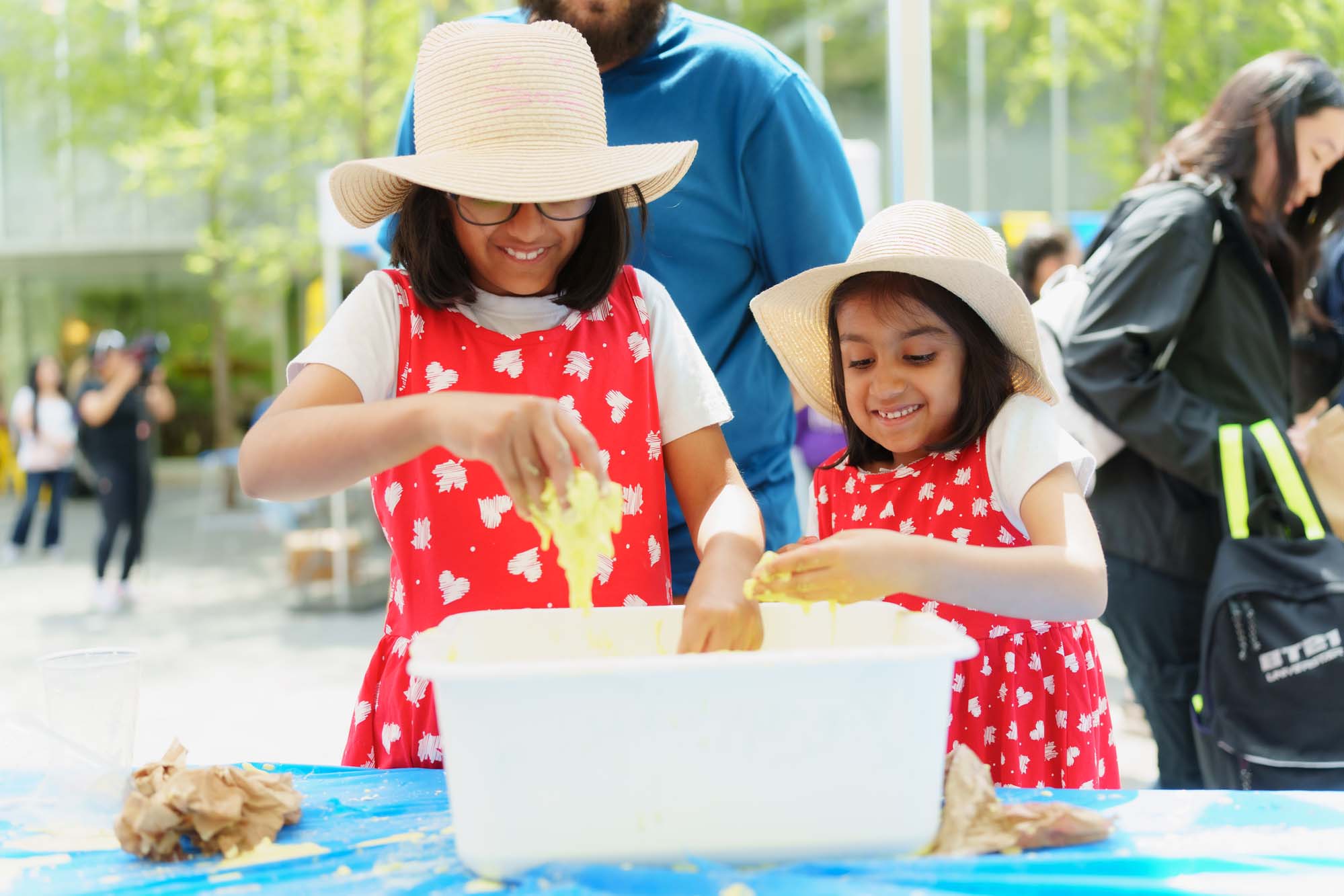 Two children playing with yellow slime with their hands in a white container at the booth.