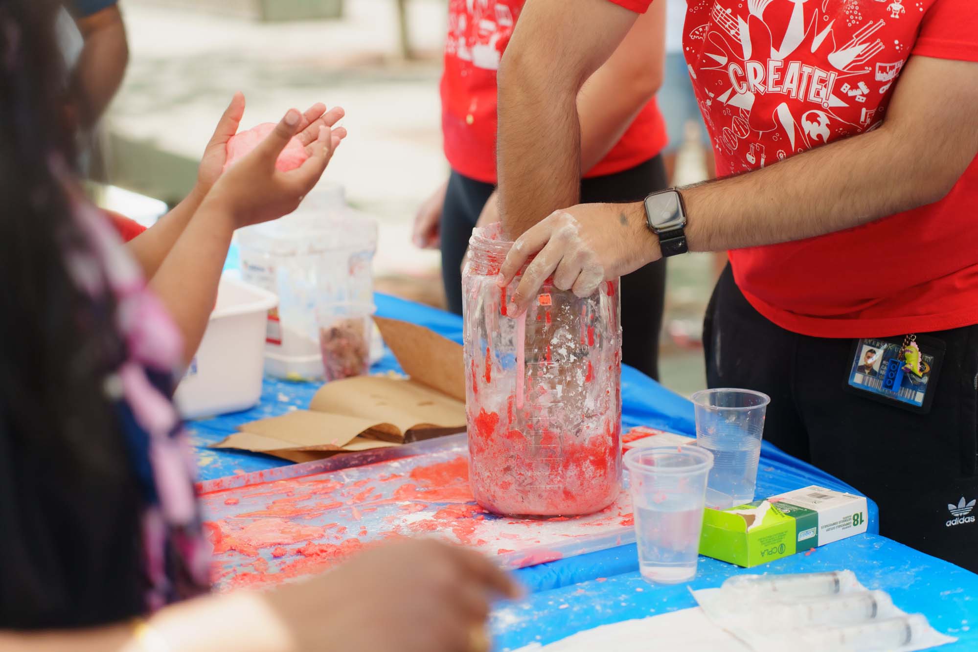 A volunteer mixing cornstarch, water and red colouring to make red slime in front of participants at the Food Science Now booth.